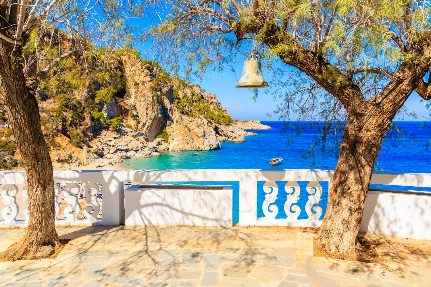 Eine am Baum hängende Glocke und Blick auf den Strand von Kyra Pynagia von der Kirchenterrasse auf Karpathos