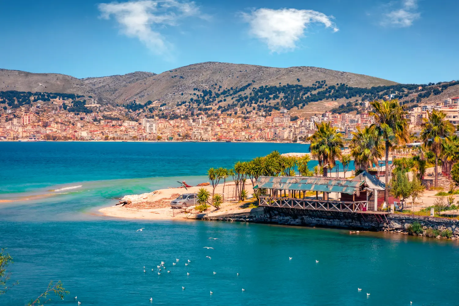 Bunte Frühling Stadtbild von Saranda Port. Exotische Landschaft mit Kiefern und die Stadt Saranda im Hintergrund