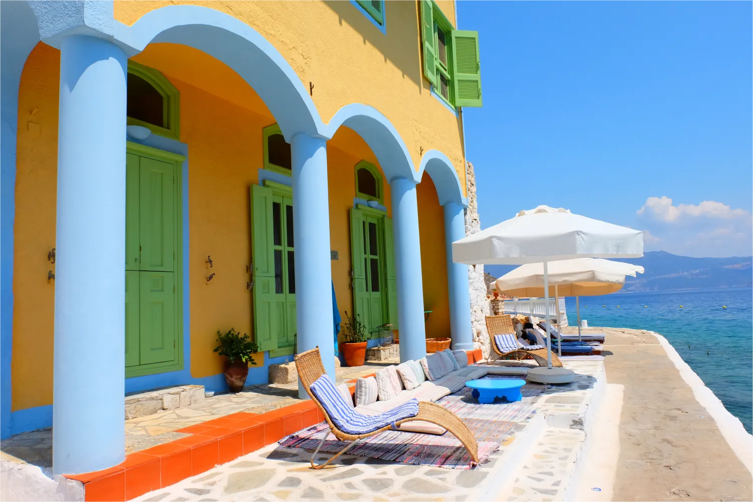 Sonnenliegen vor einem bunten Gebäude mit Blick auf das Meer in Megisti, Kastelorizo