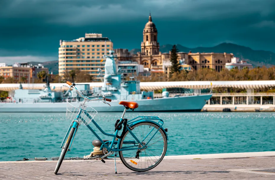 Ein hellblaues Fahrrad im Hafen von Málaga und die Kathedrale von Málaga im Hintergrund