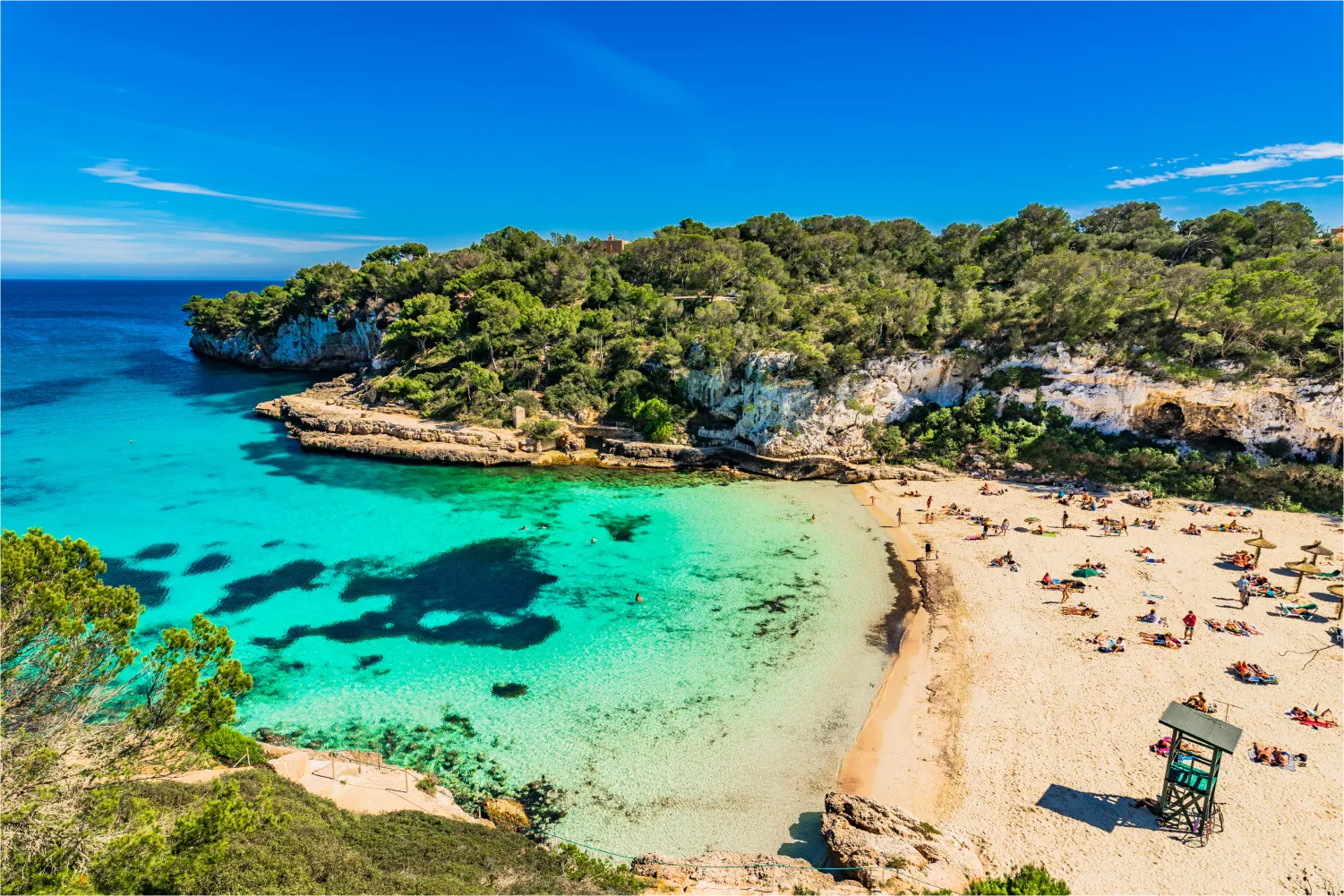 Cala Llombards auf Mallorca. Menschen sonnen sich auf dem Sand, während sie von grünen Felsklippen umgeben sind